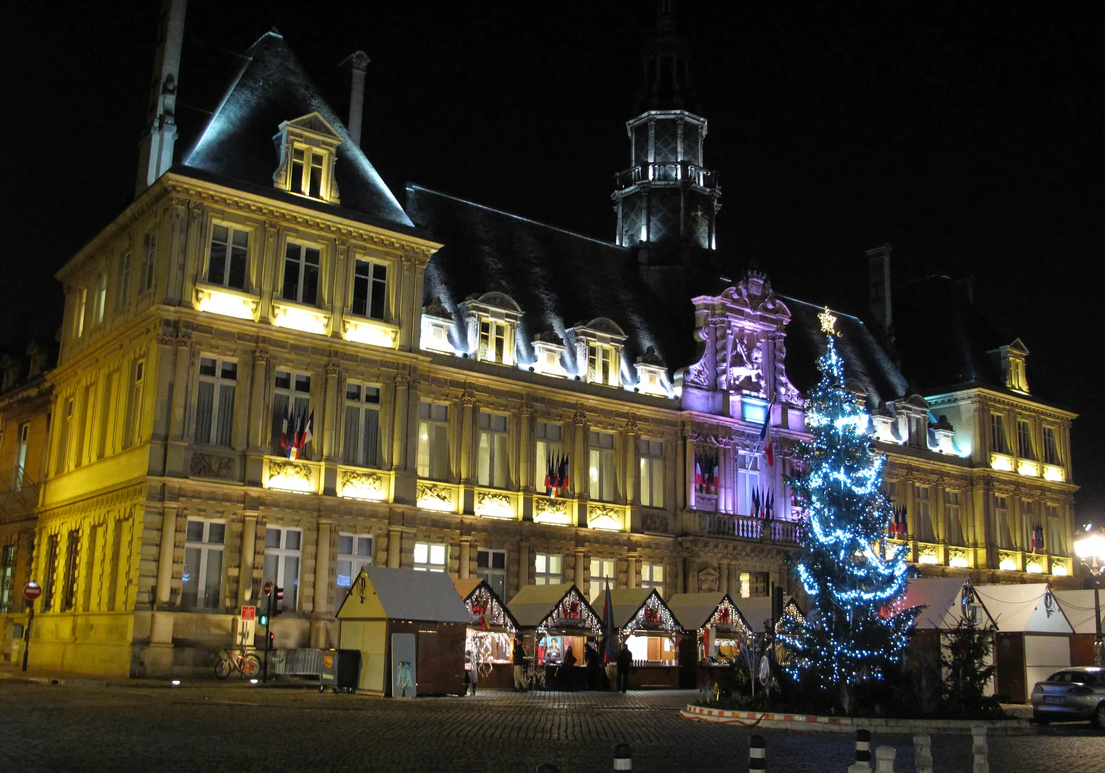 Reims town hall illuminated above Christmas stalls and a decorated tree on 3 December 2013